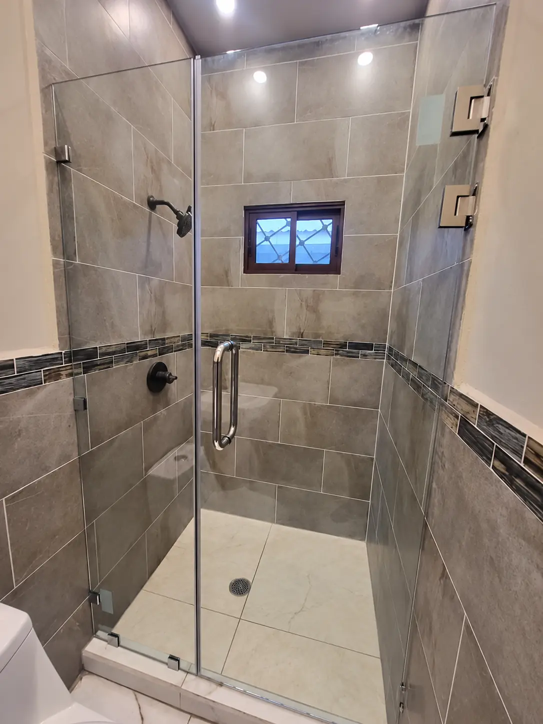 Puerta abatible de baño en vidrio templado de 10 mm con bisagras y haladera cromadas instalada por ALUR