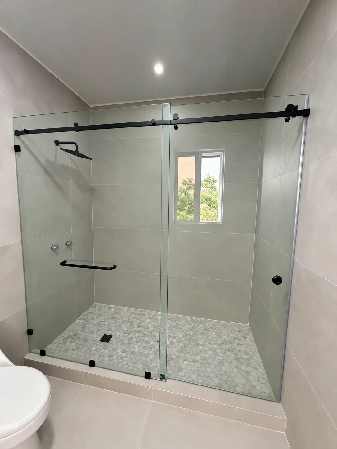 Puerta corrediza de baño en vidrio templado de 10 mm con riel y herrajes negros instalada por ALUR