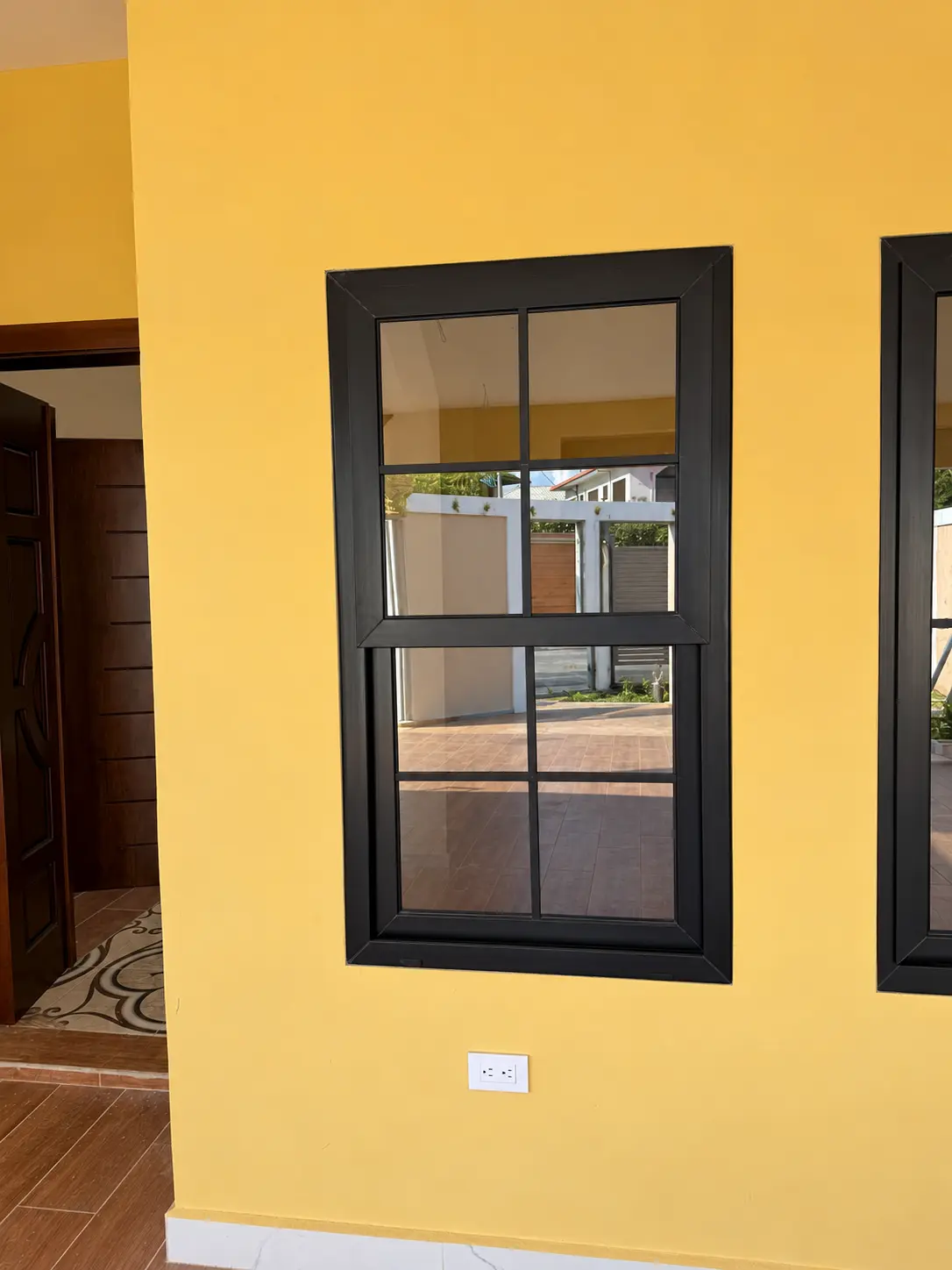 Ventana de PVC negro con divisiones decorativas en la pared de una casa amarilla, instalada por ALUR
